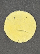 A yellow circle painted on a rough, dark asphalt surface with visible cracks and wear on the paint.