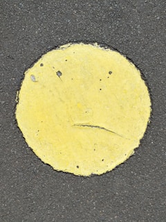 A yellow circle painted on a rough, dark asphalt surface with visible cracks and wear on the paint.