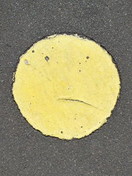 A yellow circle painted on a rough, dark asphalt surface with visible cracks and wear on the paint.