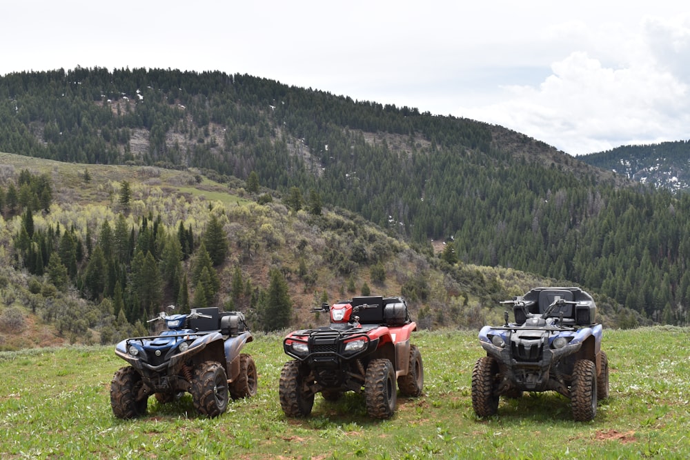 three four wheelers parked in a field with mountains in the background