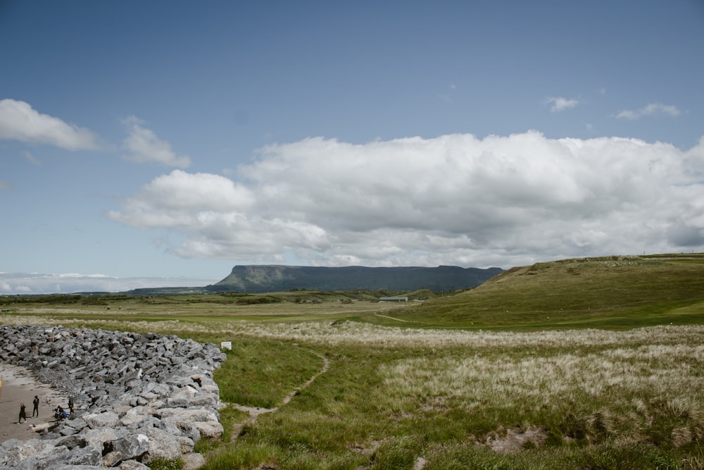 a stone wall in a grassy field with mountains in the background