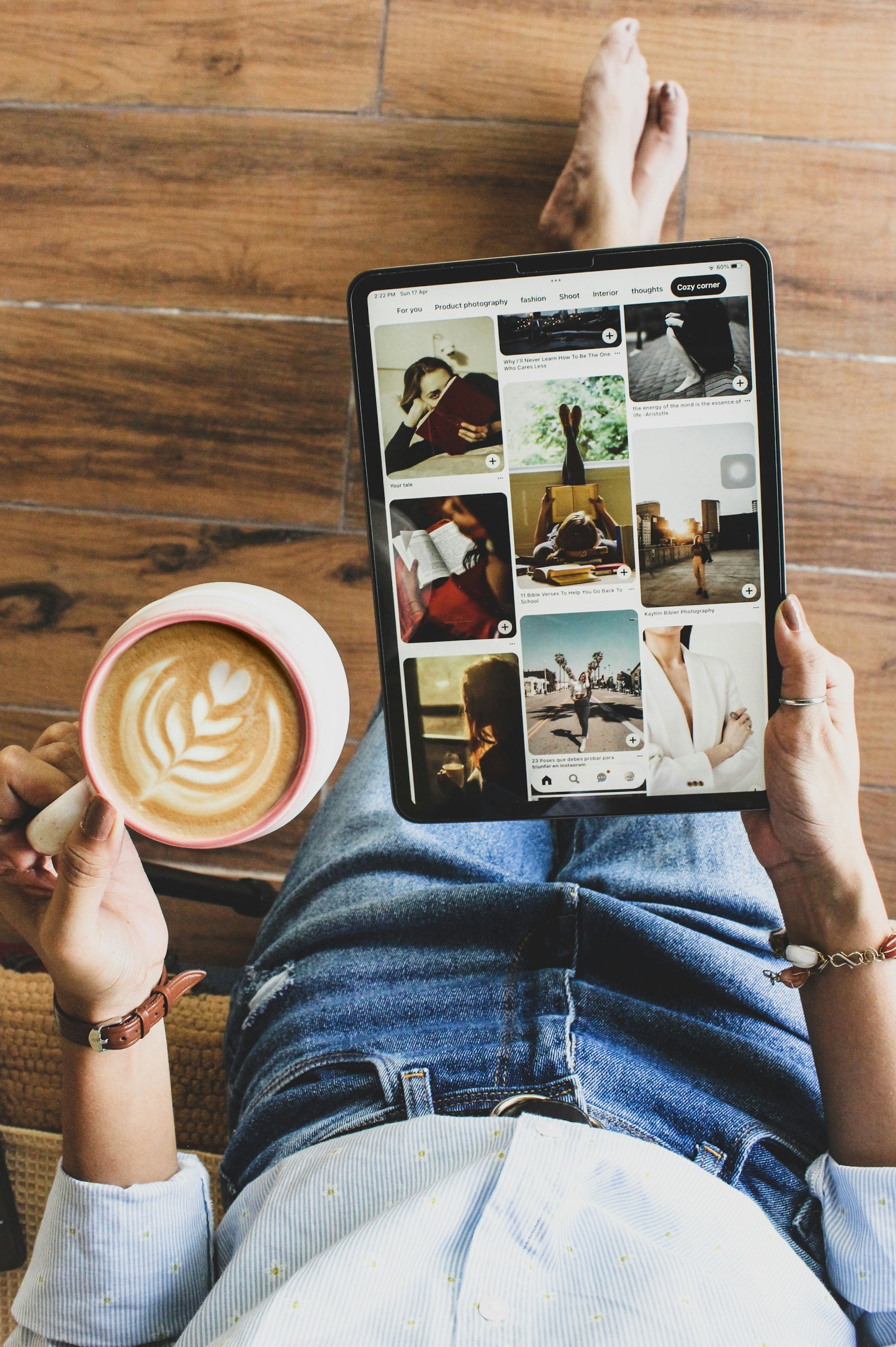 Person sits on a wooden floor holding a mug and tablet.