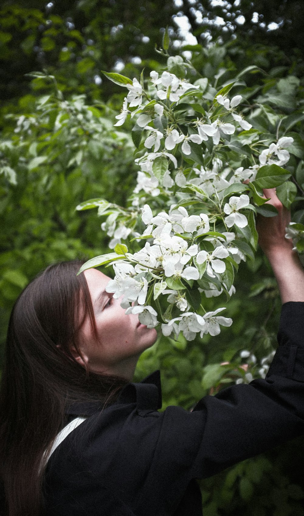 a woman is smelling a bush with white flowers