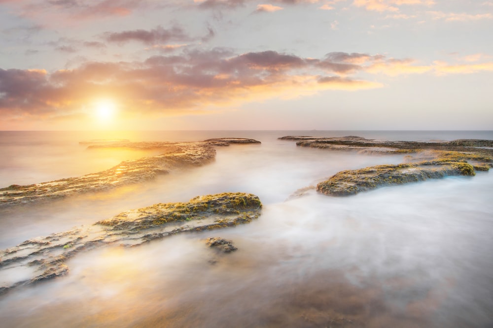 the sun is setting over a rocky beach