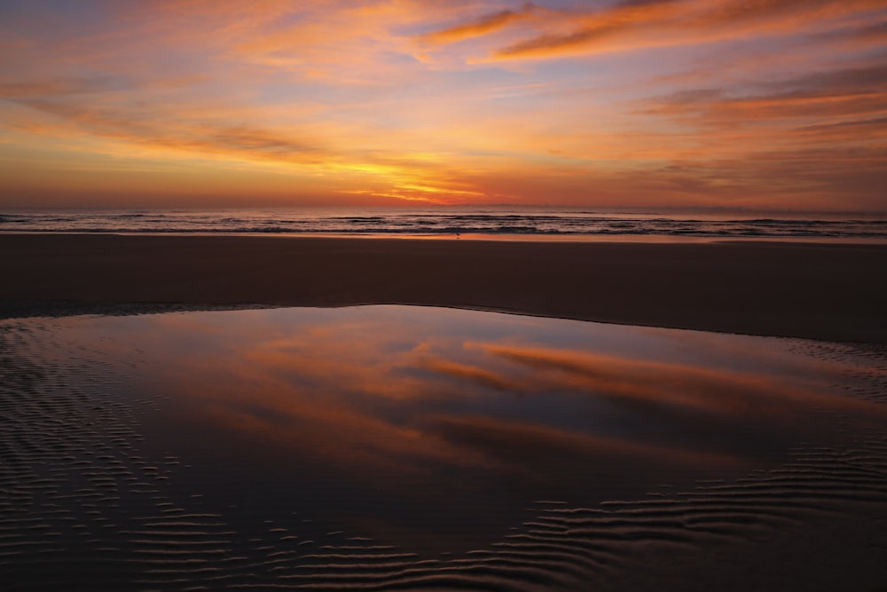 um pôr do sol sobre um corpo de água em uma praia