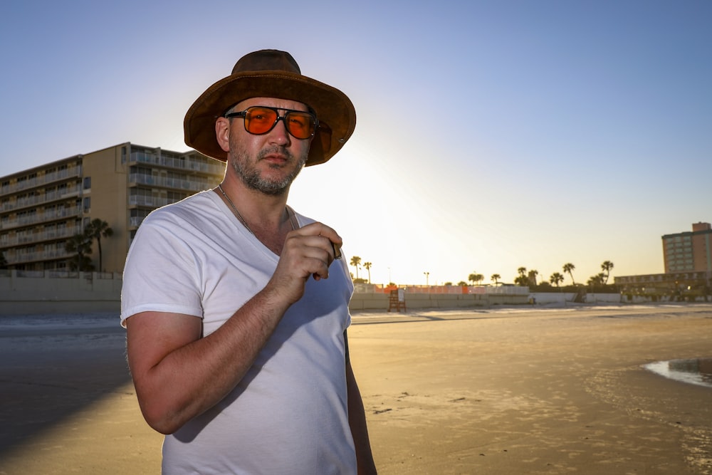 a man wearing a hat and sunglasses on the beach