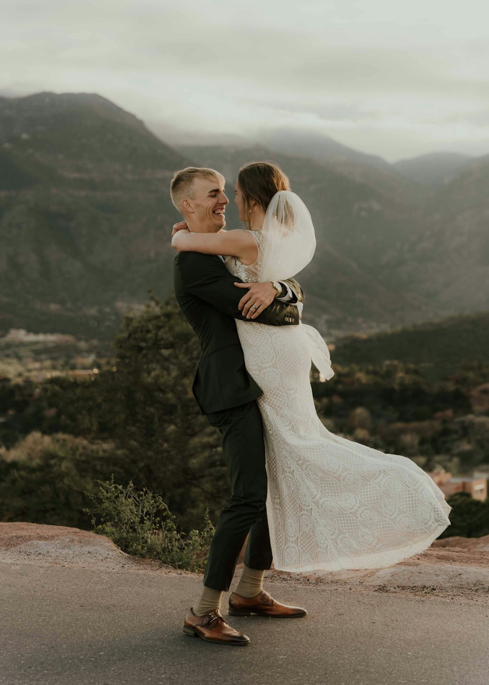 a bride and groom hugging on a mountain top