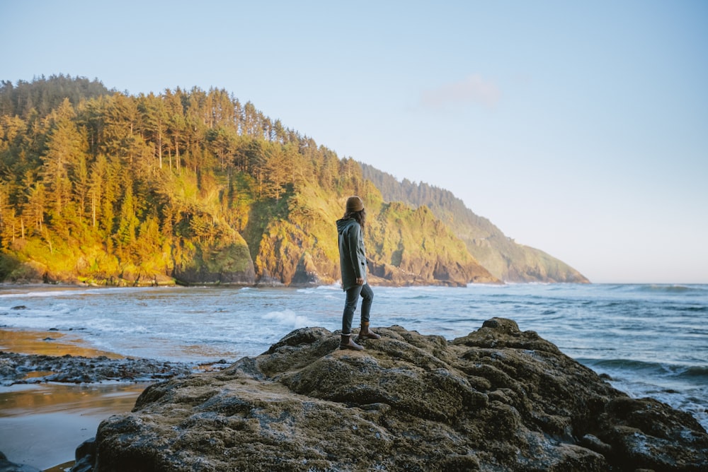 a man standing on top of a large rock near the ocean