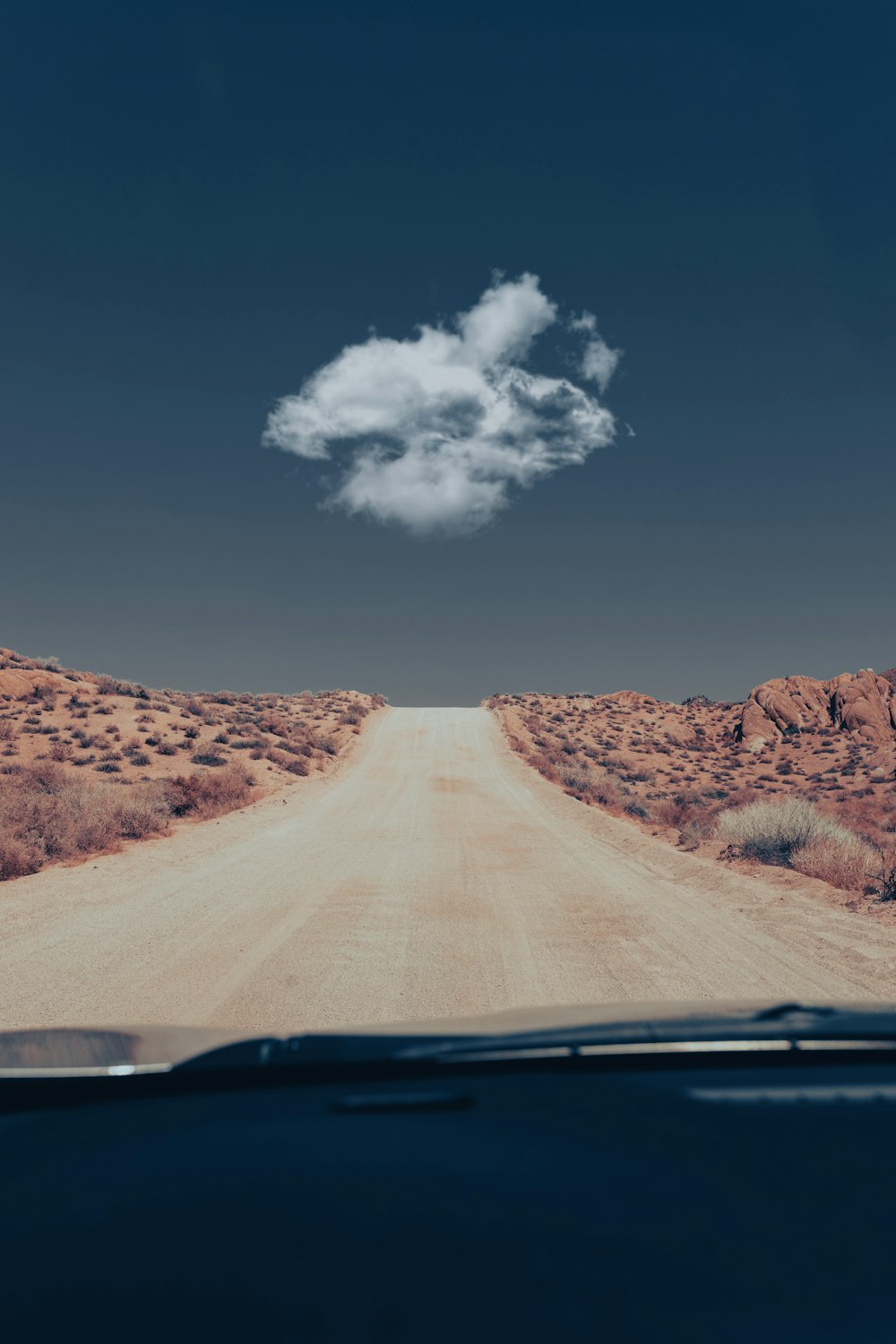a car driving down a dirt road with a cloud in the sky