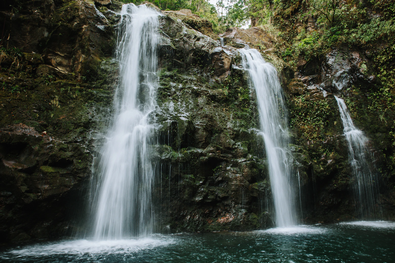A rainforest waterfall dropping between dark rock and tropical foliage on Maui