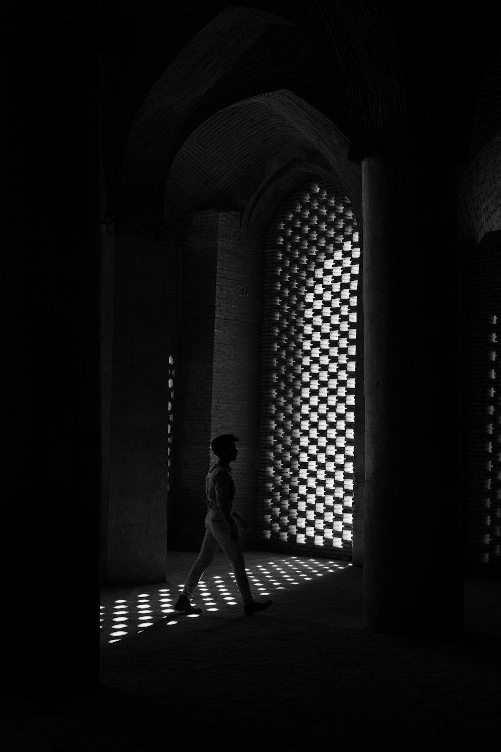 a person walking in a dark room with light coming through the windows