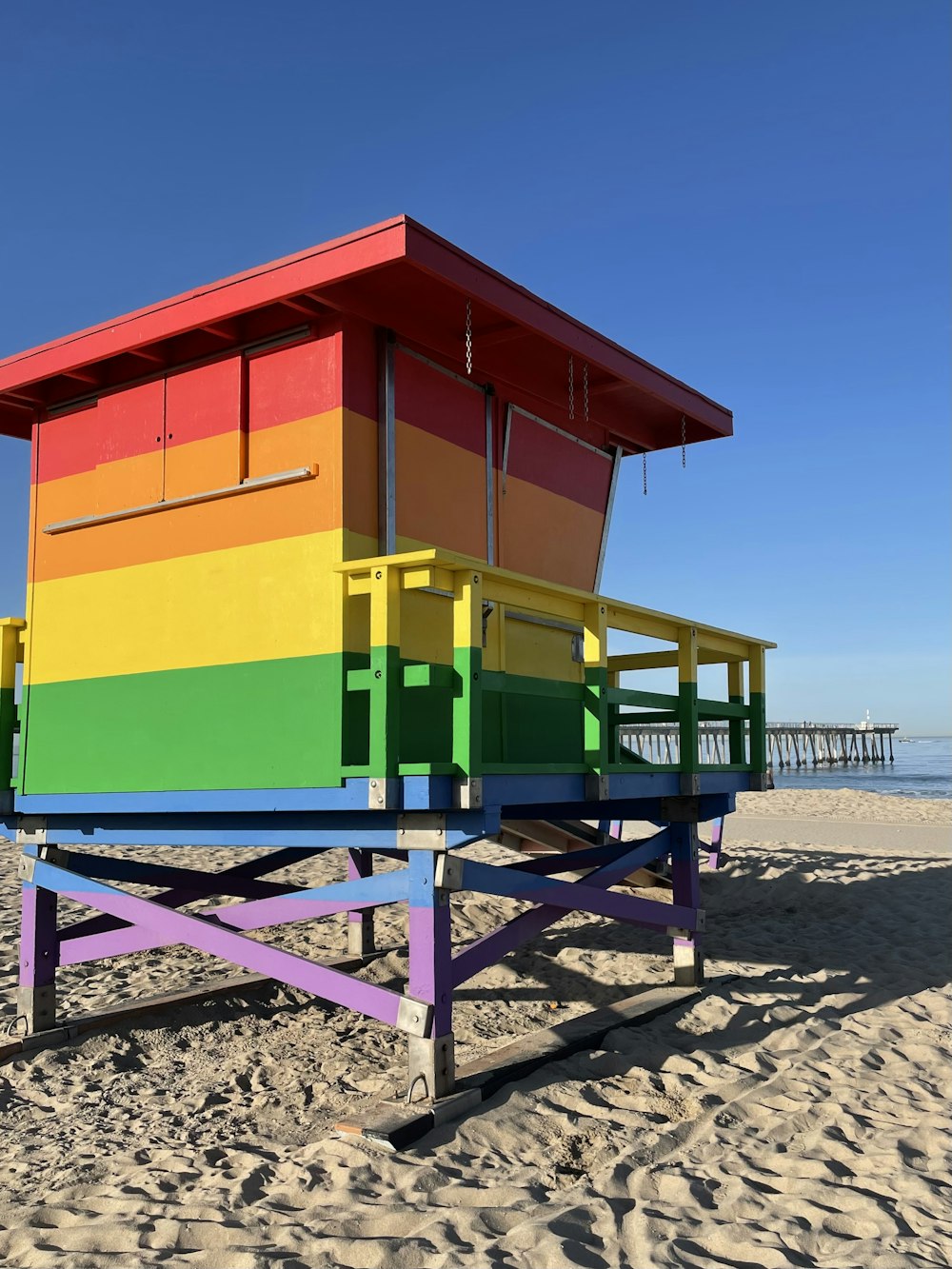 a colorful lifeguard stand on a beach with a pier in the background