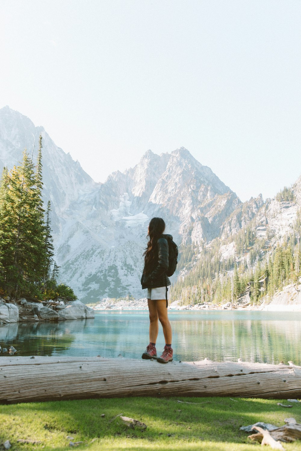 a woman standing on a log in front of a lake