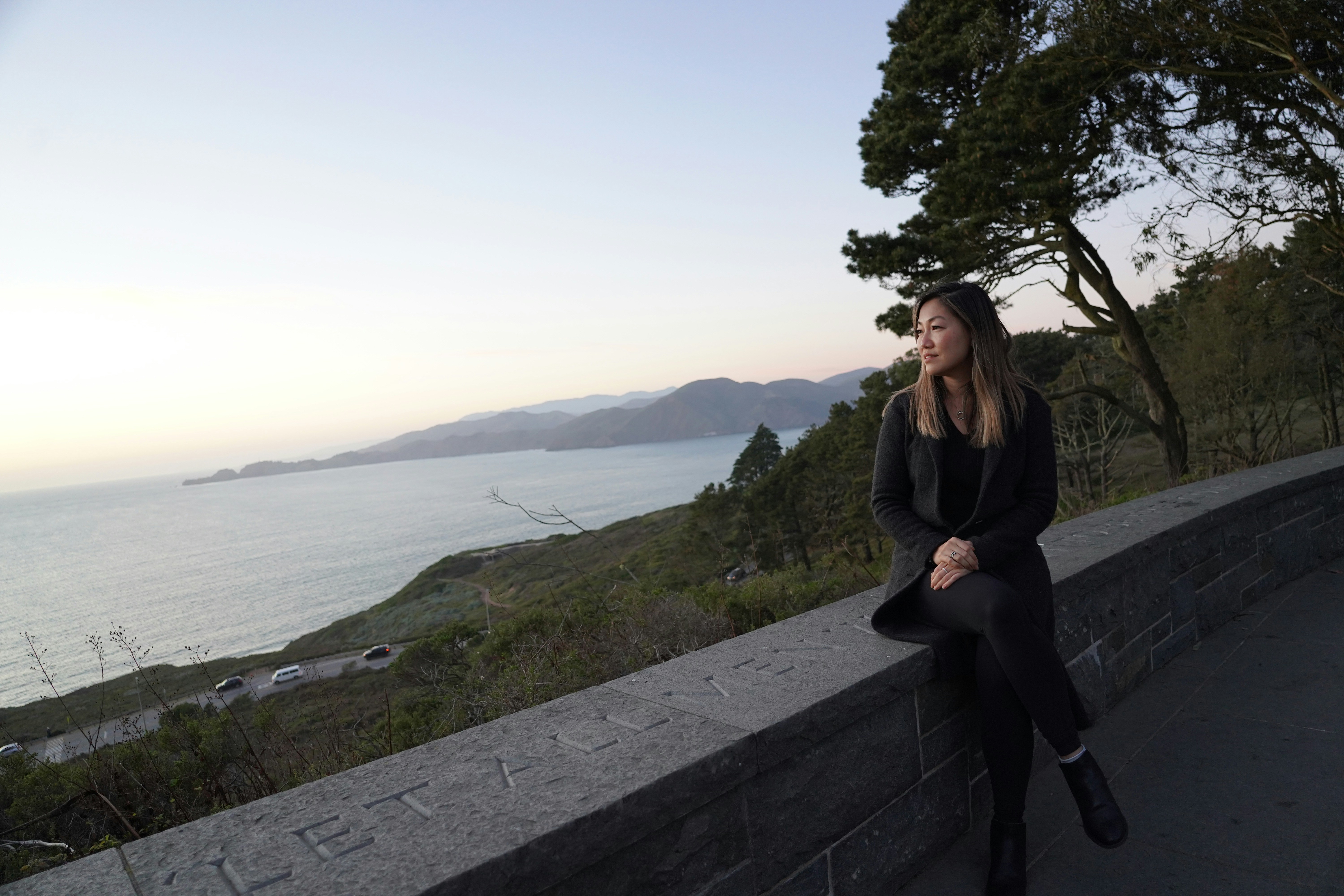 a woman sitting on a wall looking at the ocean