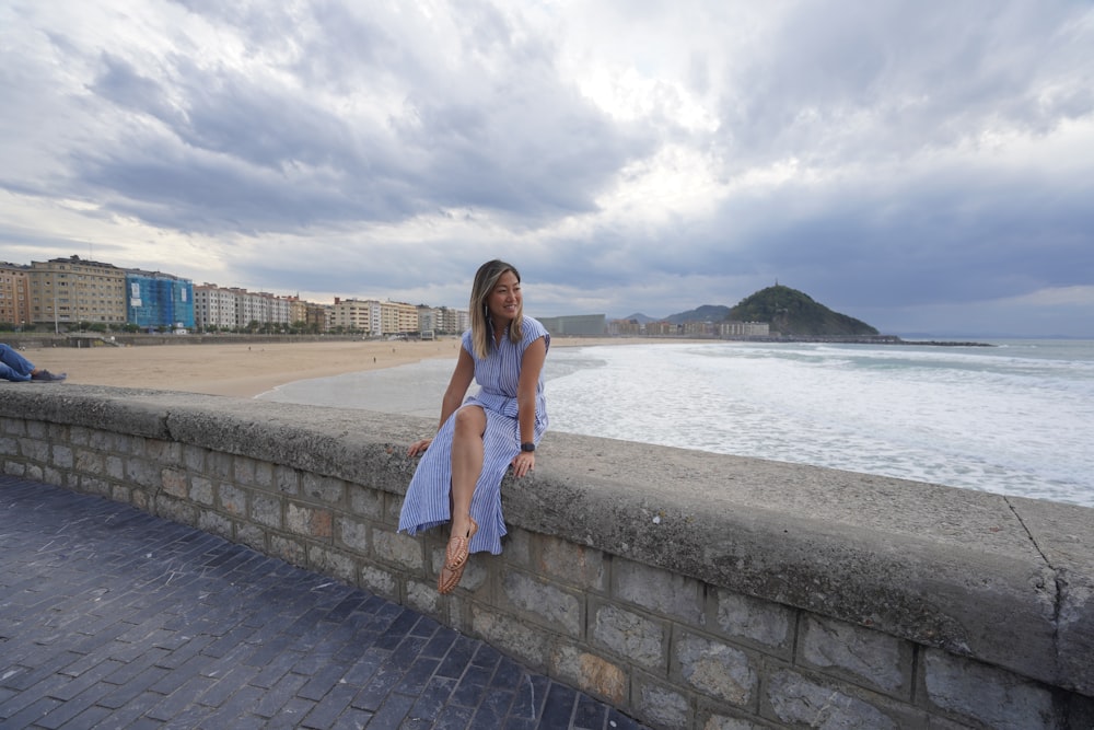 a woman sitting on a wall next to the ocean