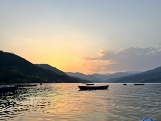 Sunset over a serene lake surrounded by green hills and small boats.