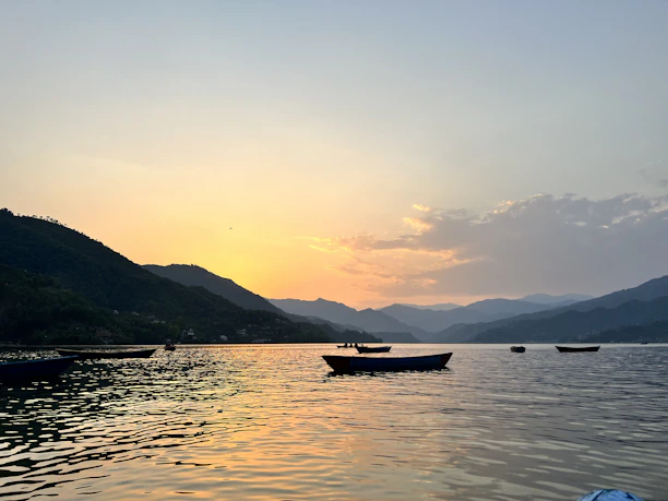 A serene lake view at sunset with colorful boats floating gently on the water.
