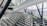 A modern architectural interior featuring large glass walls and steel beams. The structure has angular and geometric designs, with a prominent staircase or ramp intersecting the space. Natural light streams through the windows, illuminating the airy and spacious environment.