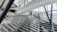 A modern architectural interior featuring large glass walls and steel beams. The structure has angular and geometric designs, with a prominent staircase or ramp intersecting the space. Natural light streams through the windows, illuminating the airy and spacious environment.
