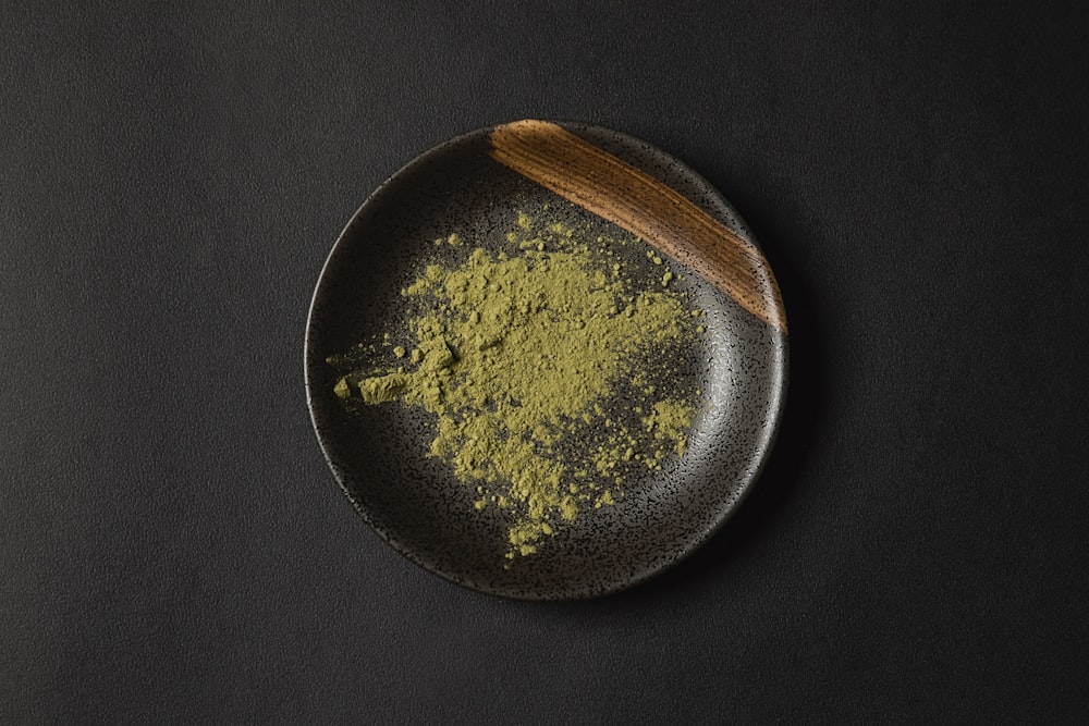 a black plate topped with green powder and a wooden spoon