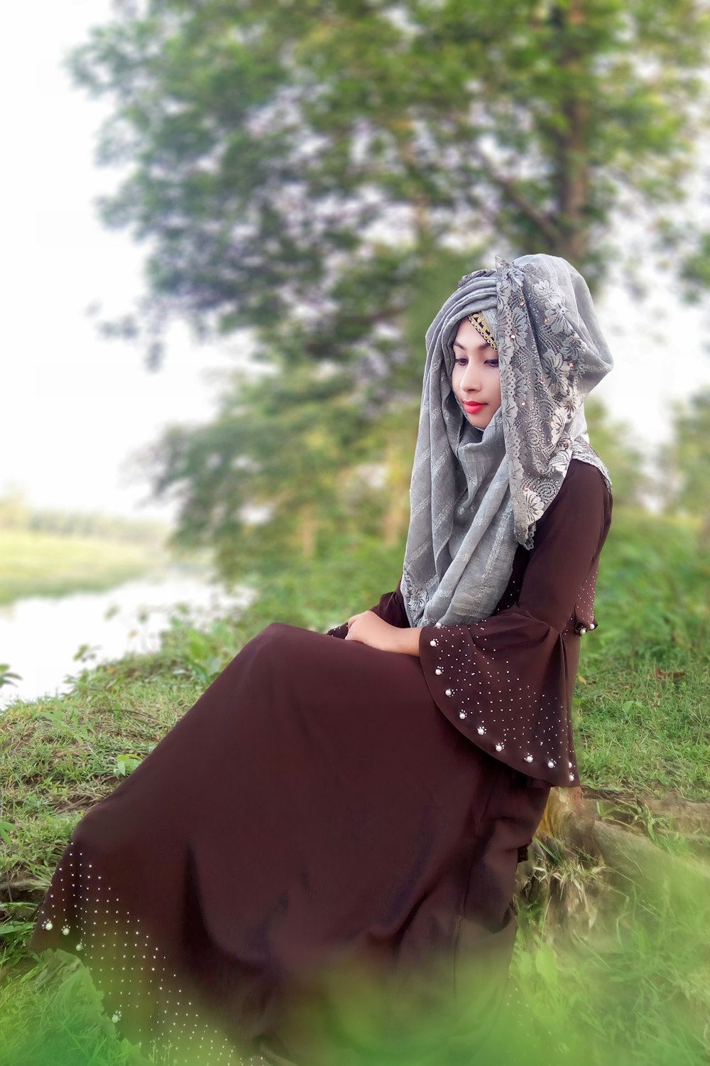 a woman in a dress and head scarf sitting in the grass