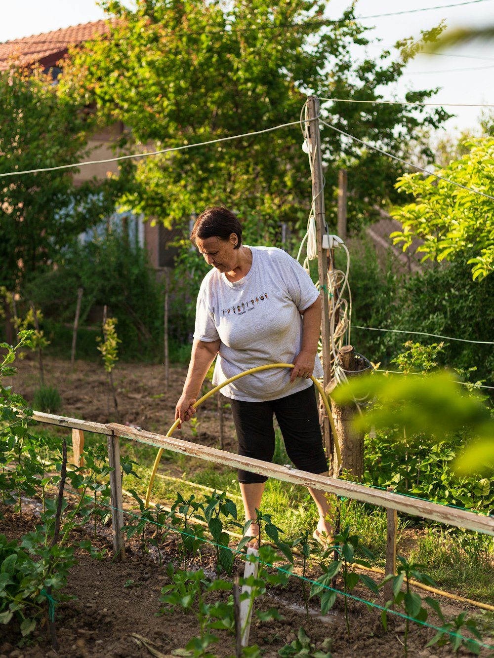 a woman in white shirt holding a garden hose