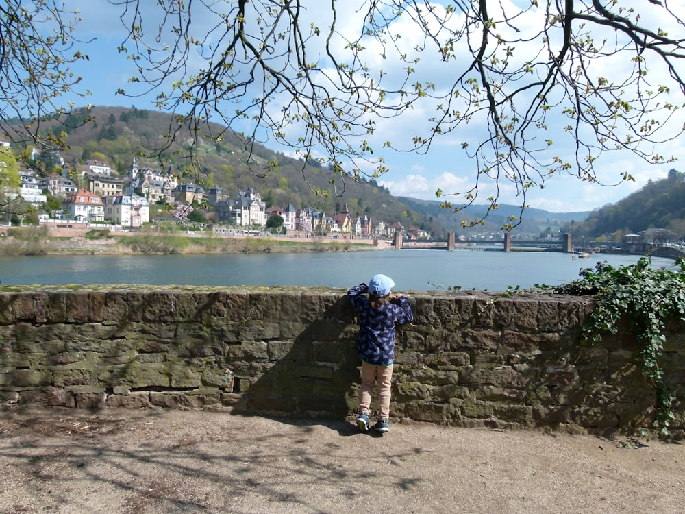 a person leaning against a stone wall near a body of water