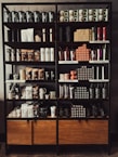 A neatly organized store shelf displaying various branded merchandise including coffee mugs, tumblers, bags of coffee beans, and cups. The products are arranged in a visually appealing manner with different collections and themes.