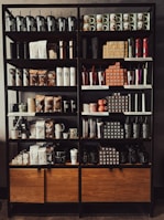 A neatly organized store shelf displaying various branded merchandise including coffee mugs, tumblers, bags of coffee beans, and cups. The products are arranged in a visually appealing manner with different collections and themes.