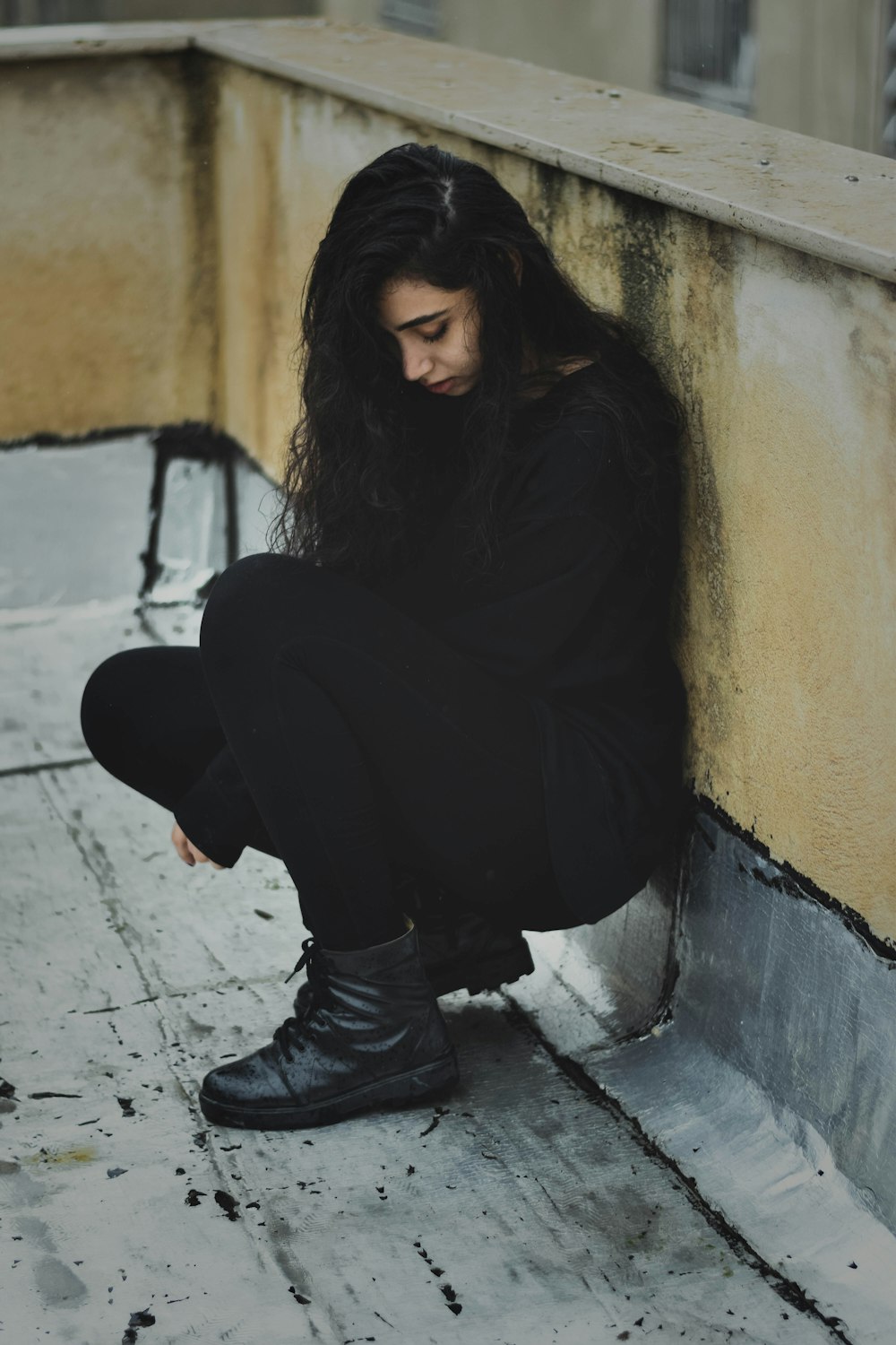 a woman with long hair sitting against a wall