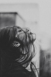 a black and white photo of a woman with her hair blowing in the wind