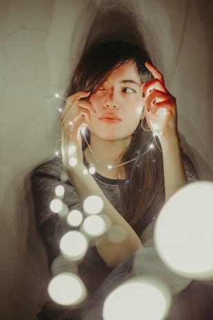 A softly lit portrait of a photographer surrounded by glowing fairy lights in a dark forest.