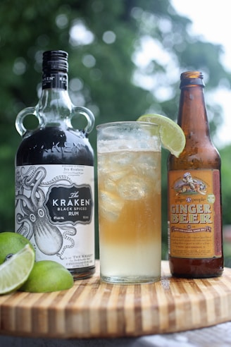 A dark rum bottle with a glass of rum on the rocks and tropical fruits around