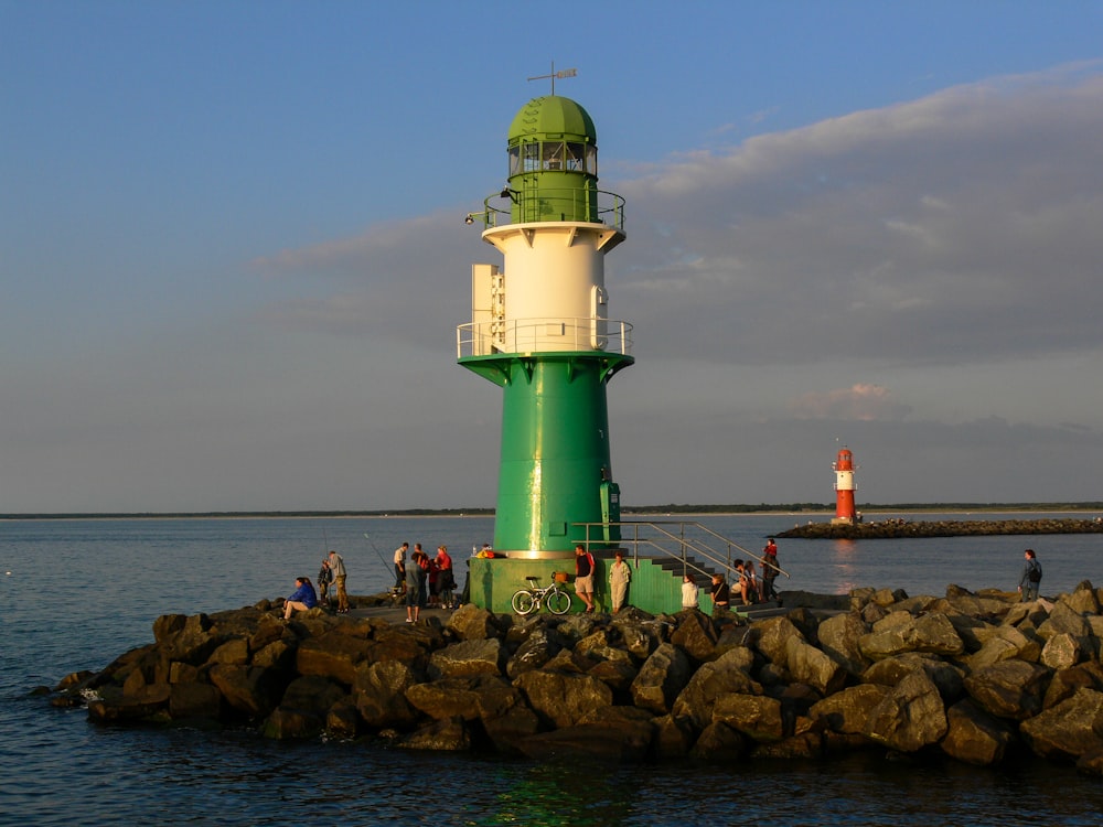 a group of people standing around a green and white lighthouse