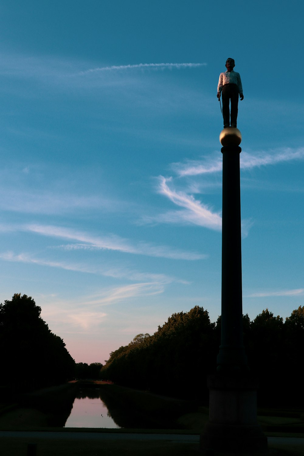 a man standing on top of a tall pole next to a body of water