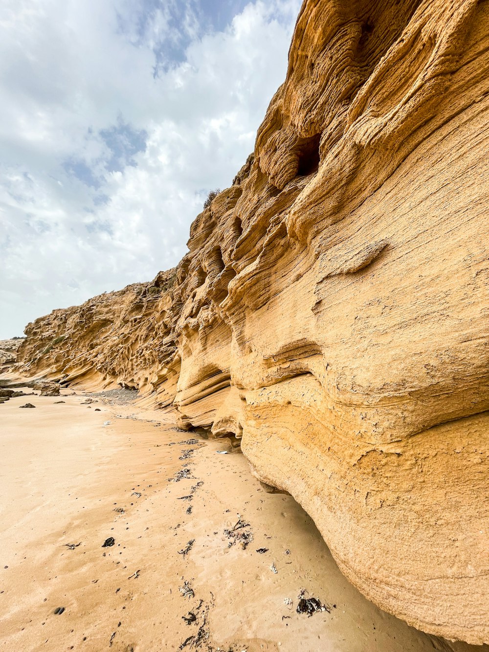 a sandy beach next to a cliff under a cloudy sky