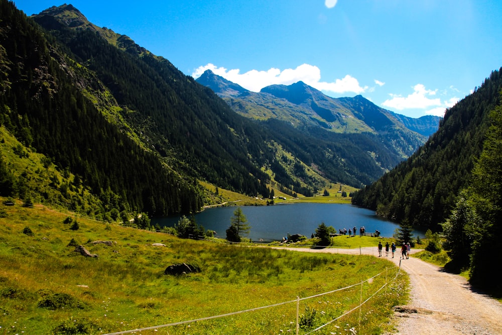 a group of people walking down a dirt road next to a lake