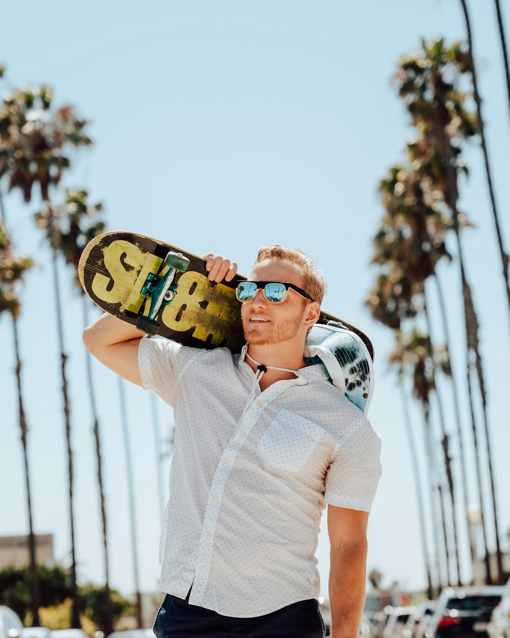 a man holding a skateboard in front of palm trees
