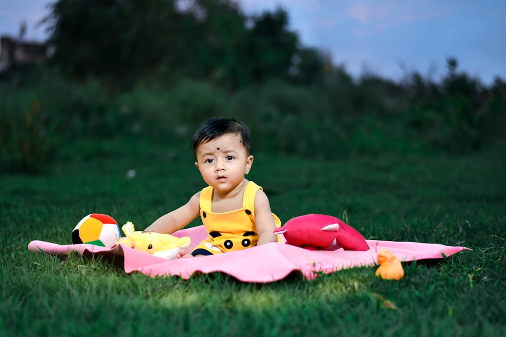 a baby sitting on a pink blanket in the grass