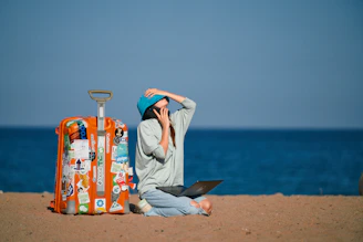 a person sitting on a beach with a suitcase and a laptop