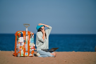 a person sitting on a beach with a suitcase and a laptop