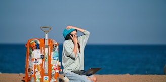 a person sitting on a beach with a suitcase and a laptop
