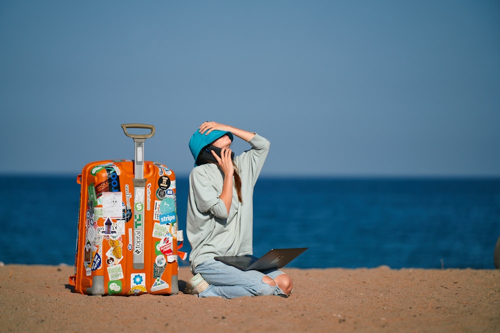 una persona seduta su una spiaggia con una valigia e un computer portatile