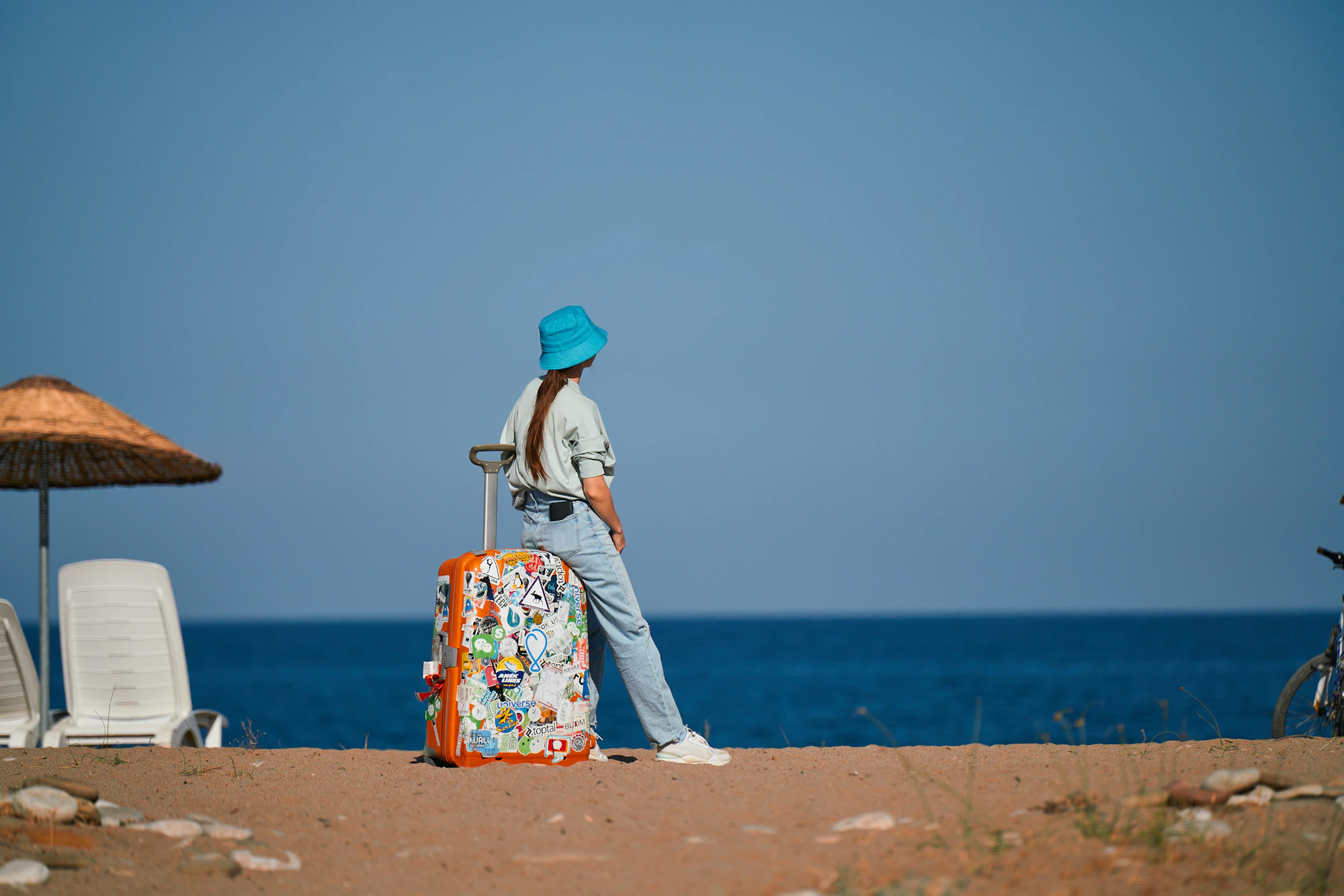 Mulher em uma praia ao entardecer com uma mala de viagem — imagem ilustrativa