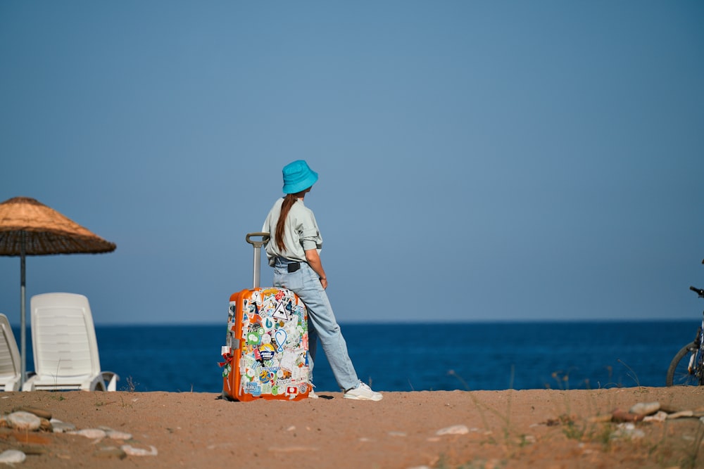 a woman standing on a beach with a suitcase