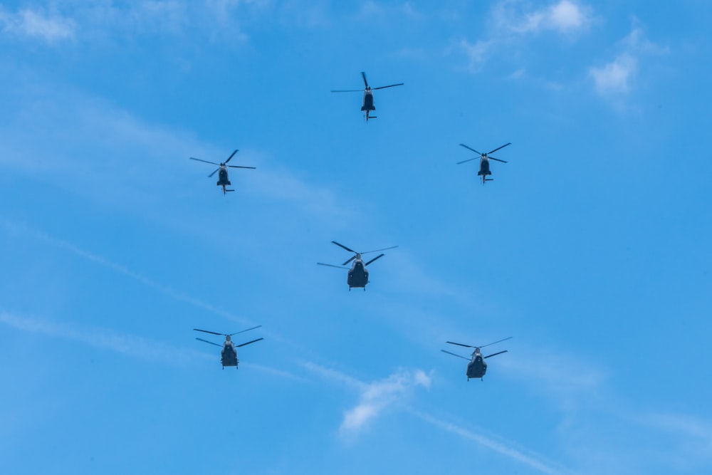 a group of military helicopters flying through a blue sky