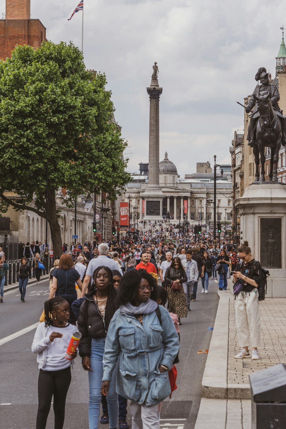 a crowd of people walking down a street next to a statue