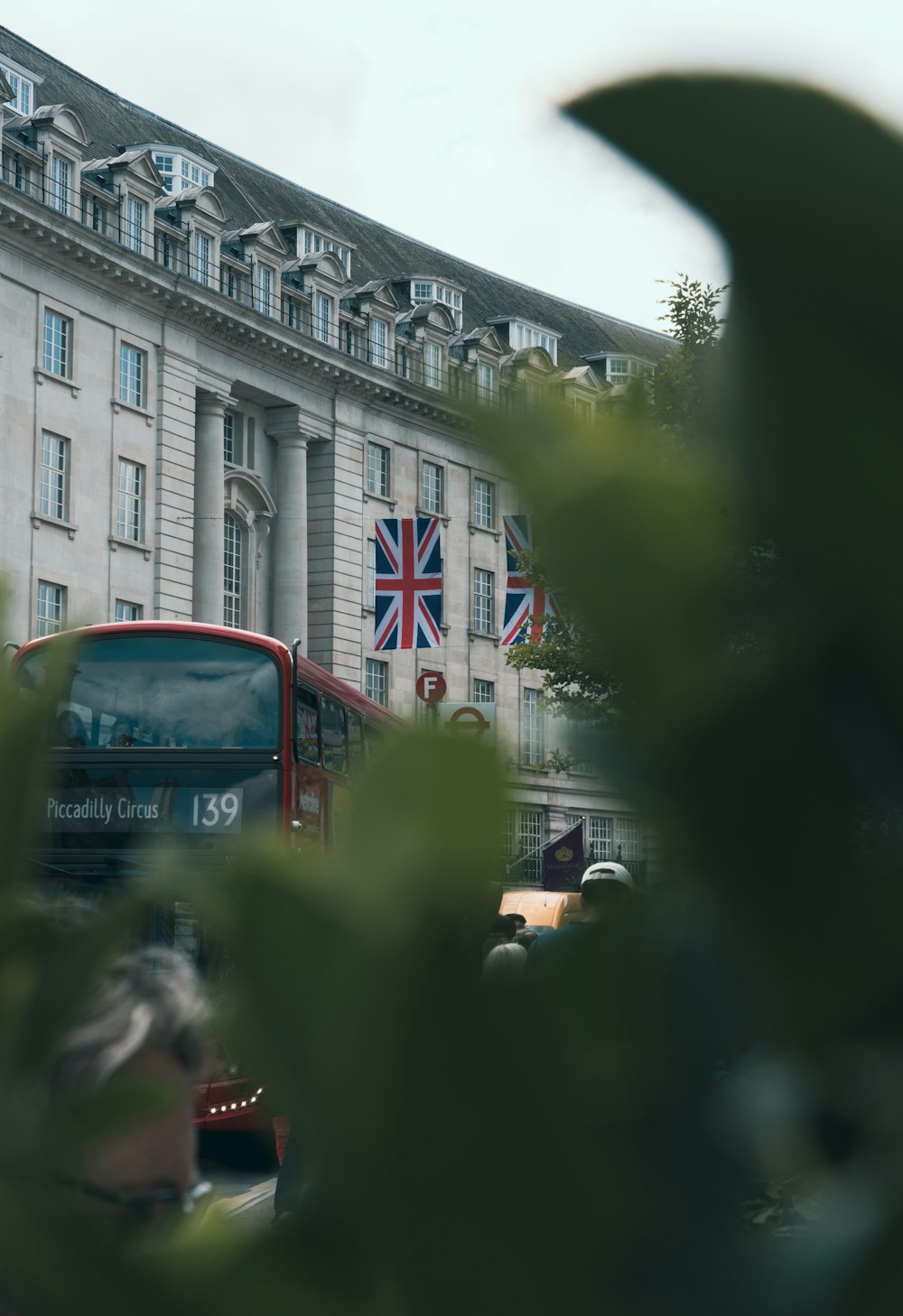 a red double decker bus driving past a tall building