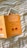 A book with an orange cover featuring the title in German by John Gray, next to an image partially tucked inside it. The background is a white fabric with yellow and gray stripes.