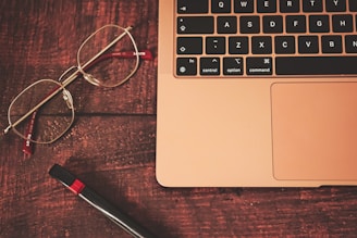 a pair of glasses sitting on top of a wooden table next to a laptop computer